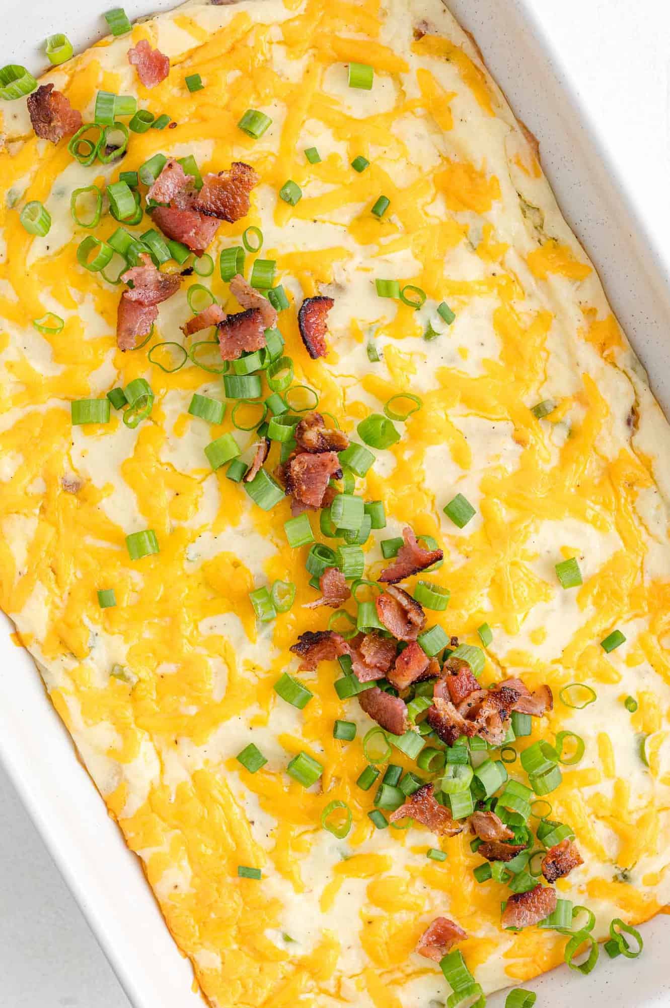 Mashed potato casserole topped with bacon and green onions.