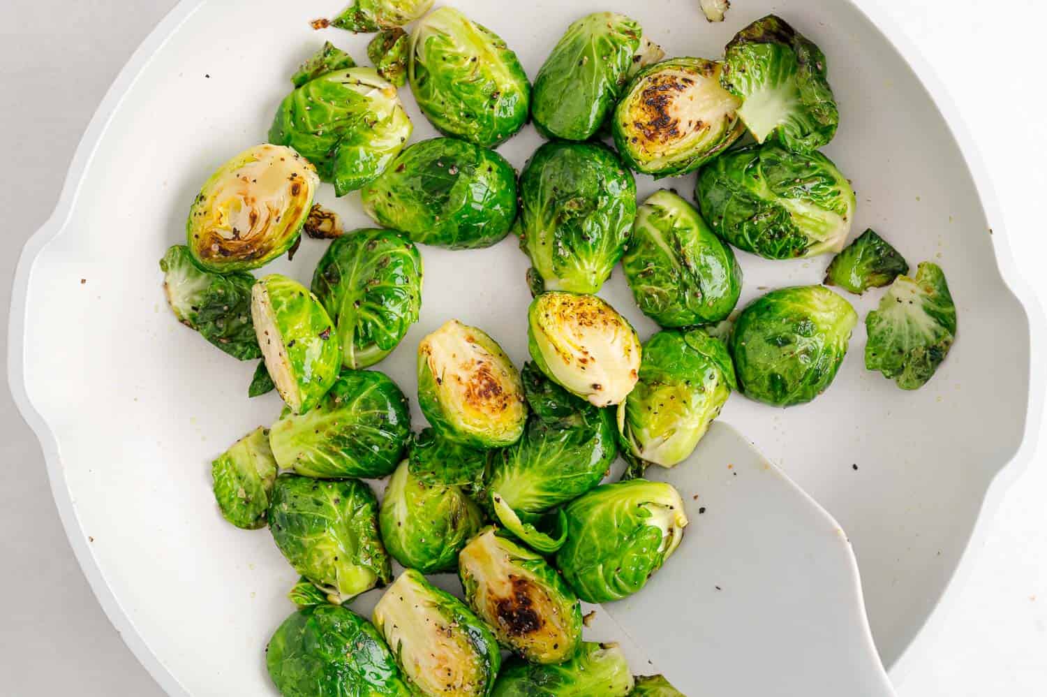 Brussels sprouts in a frying pan being stirred.