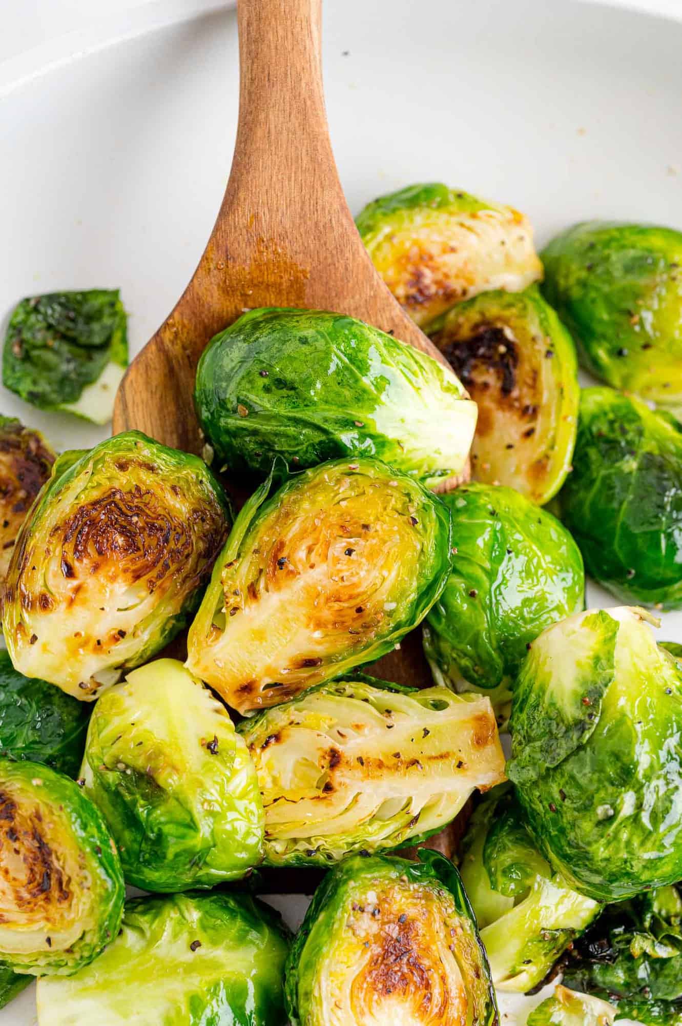 Brussels sprouts in a frying pan with a wooden spoon.