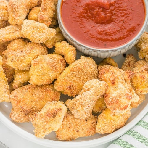 Healthy chicken nuggets on a plate with pizza sauce.