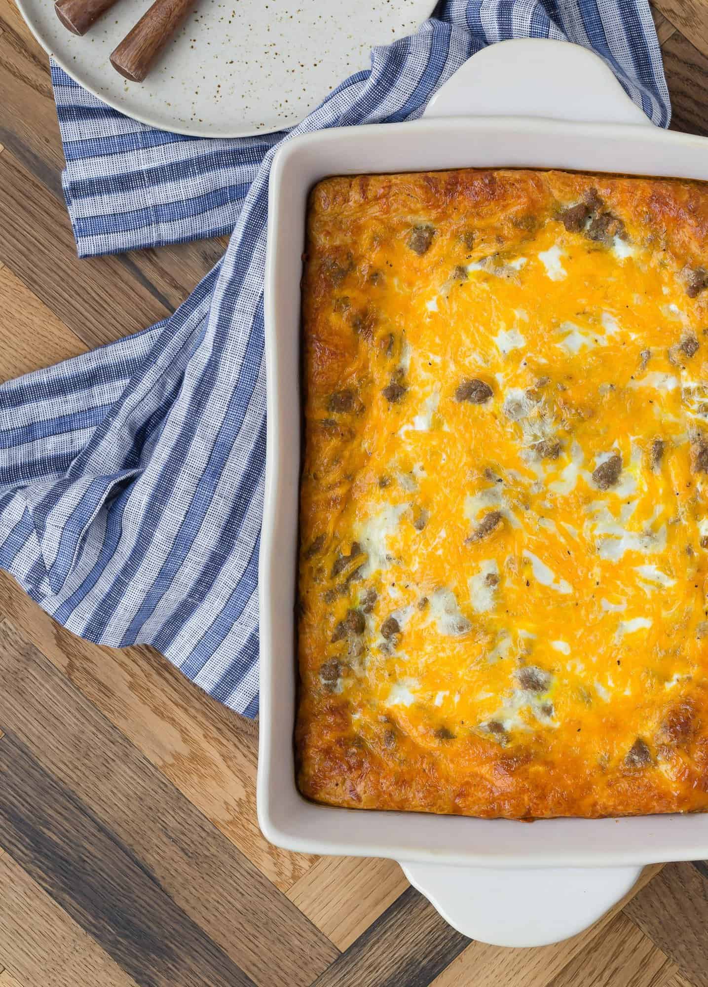 Overhead view of a pan of breakfast casserole placed on a blue striped linen and a wooden background.