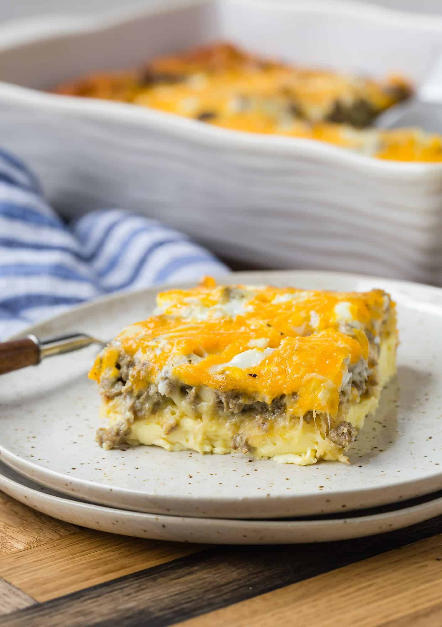 Slice of breakfast casserole on a plate. Layers of egg, crescent roll, sausage, and cheese are visible.