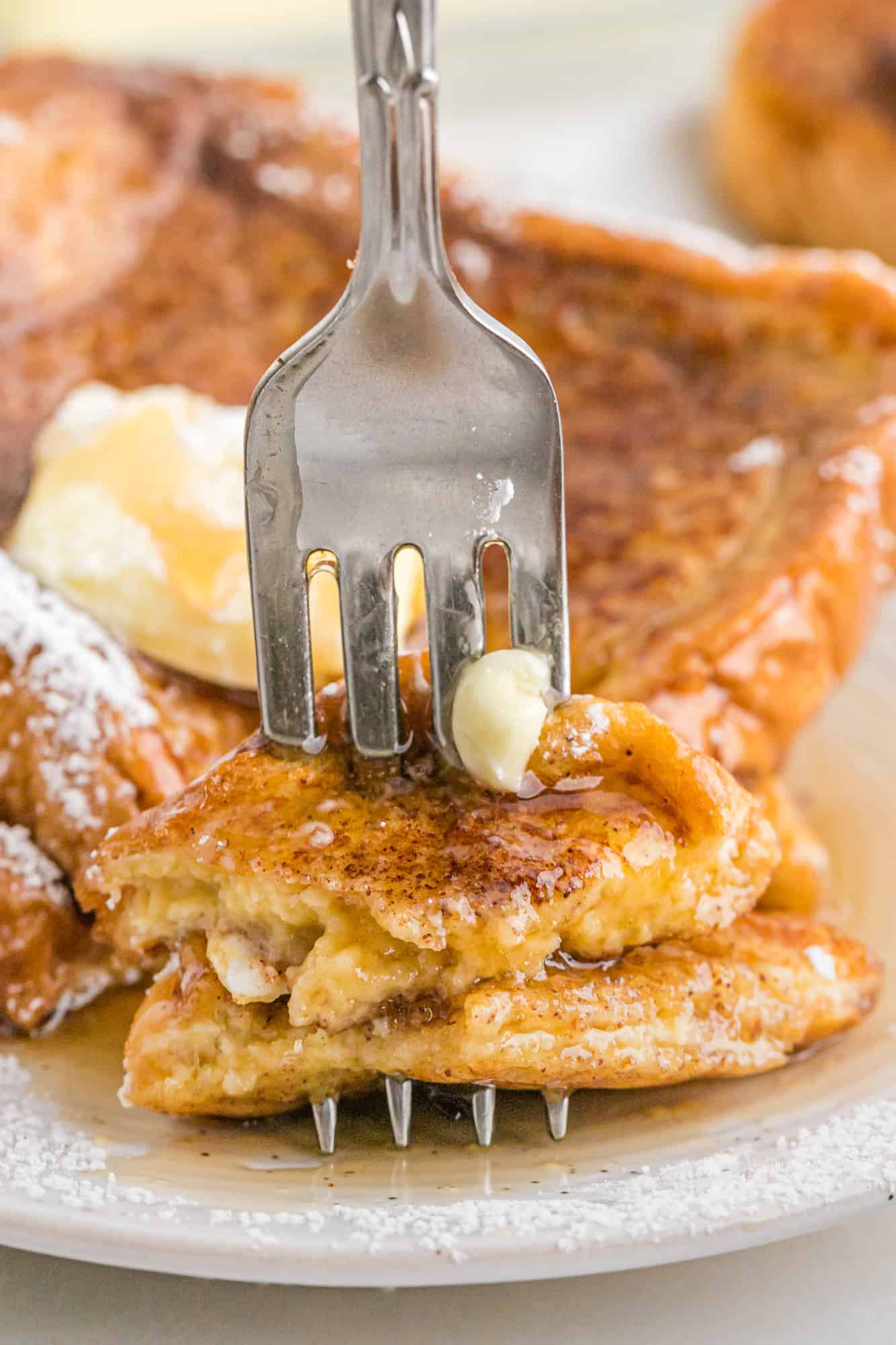 A fork stuck into a slice of French toast to show the texture.