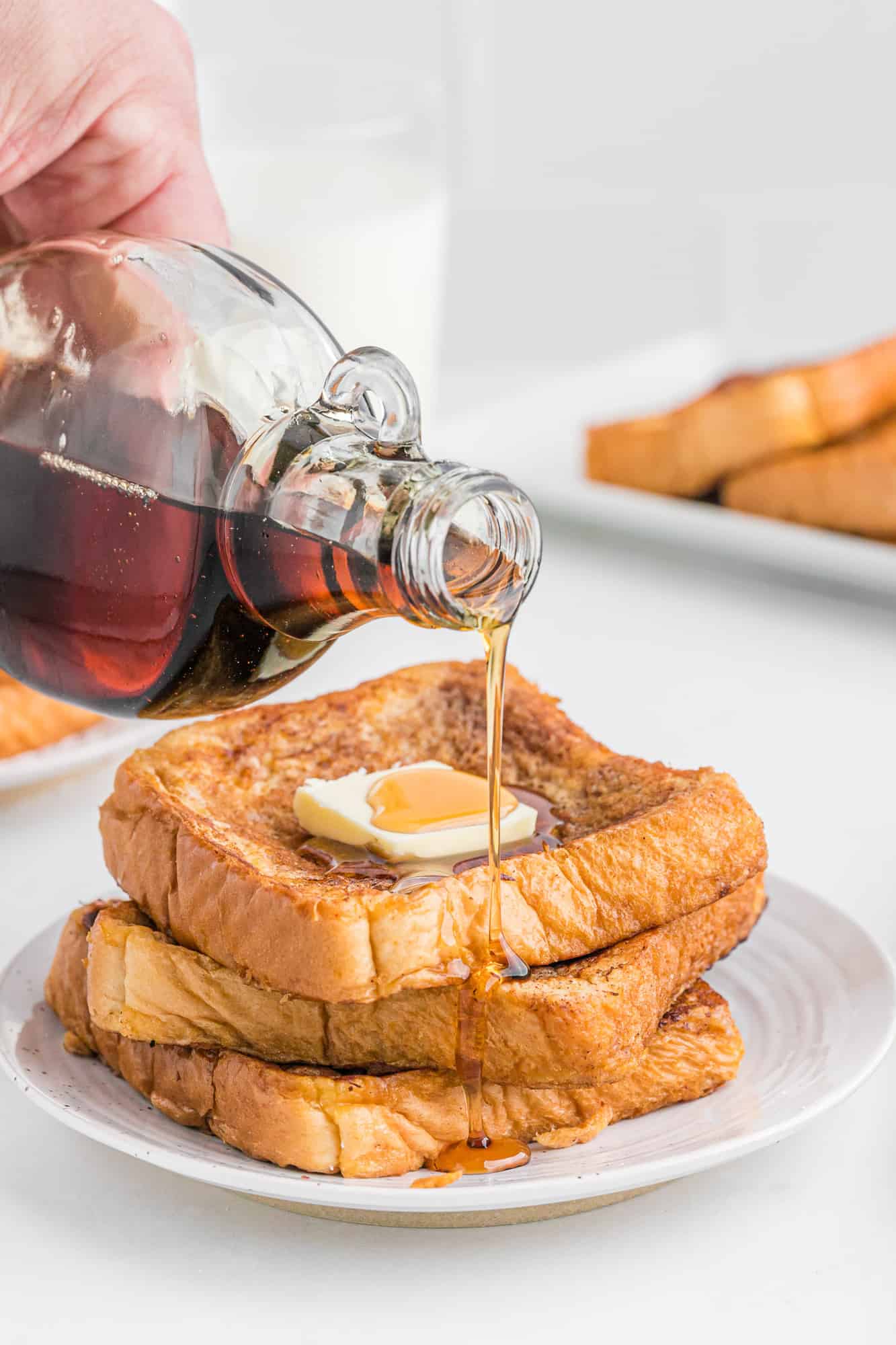 Maple syrup is drizzled over top of a stack of French toast topped with butter on a plate.