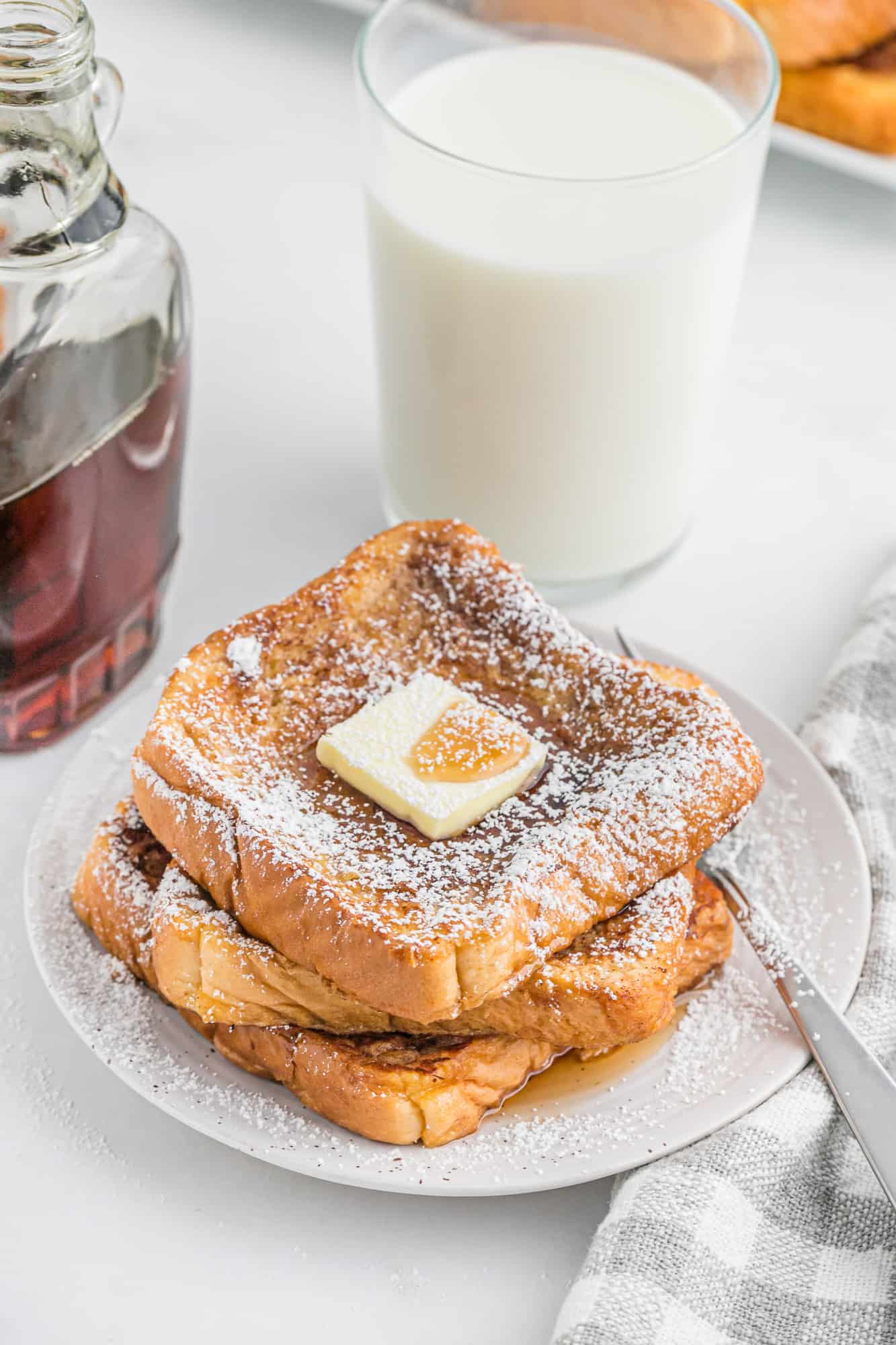 French toast stacked on a plate with powdered sugar, butter, and maple syrup.