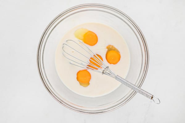 Eggs and milk in a bowl with a whisk.