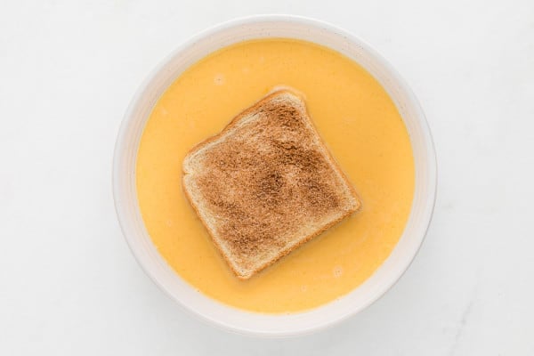 A bread slice dipped in a bowl of egg mixture.