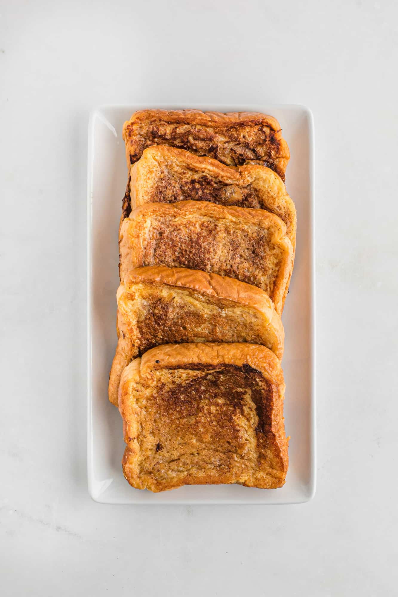 A row of cooked French toast slices lined up on a plate.
