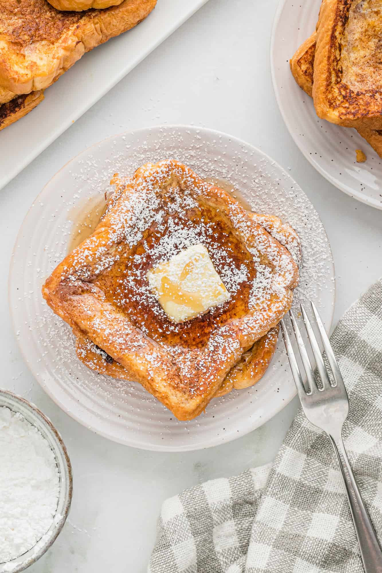 Classic french toast on a white plate with butter, syrup, and powdered sugar.