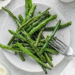 Roasted green beans on a round white plate.