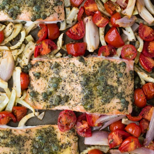 Close up view of salmon with dill and capers, surrounded by vegetables.