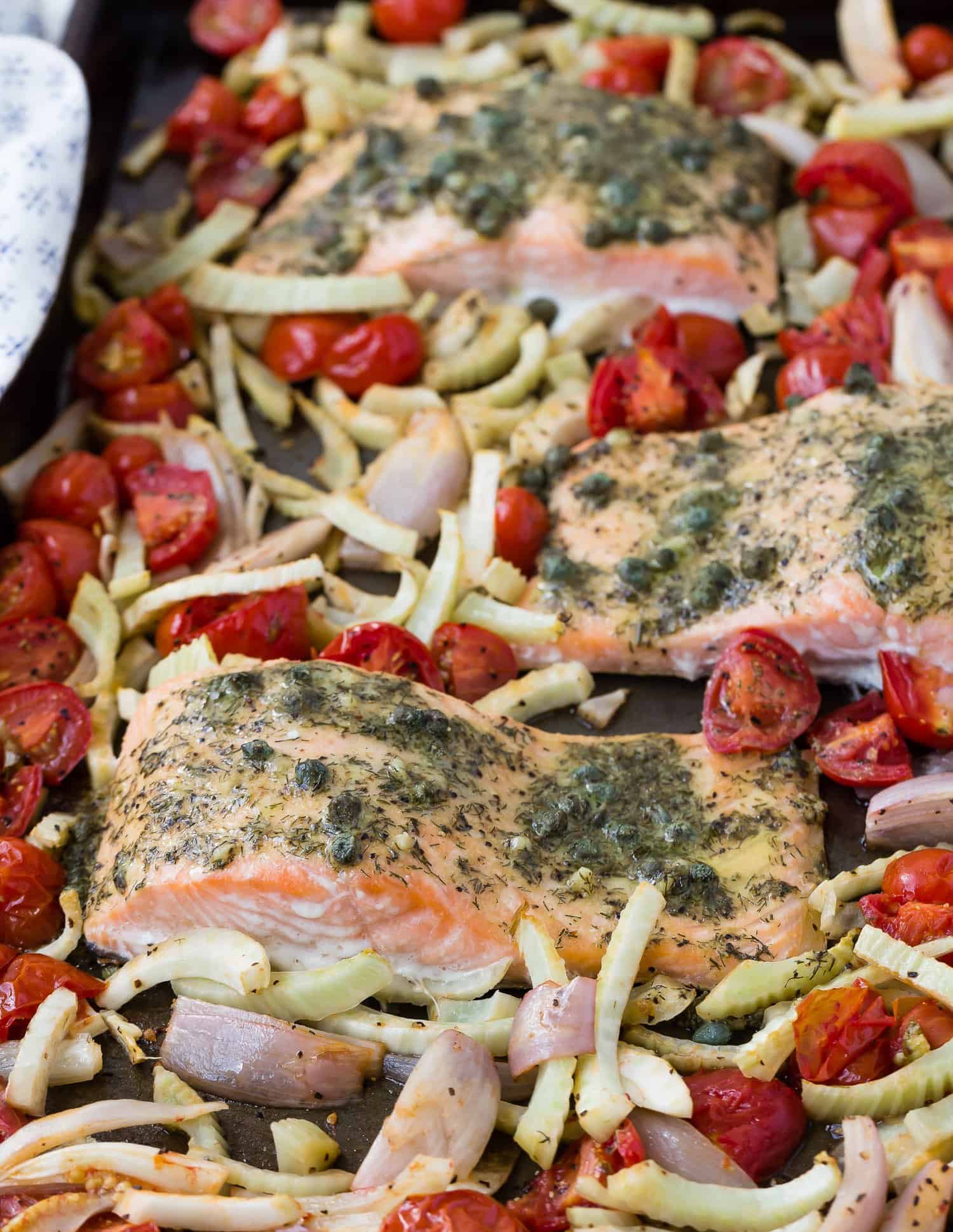 Salmon a sheet pan surrounded by roasted vegetables,