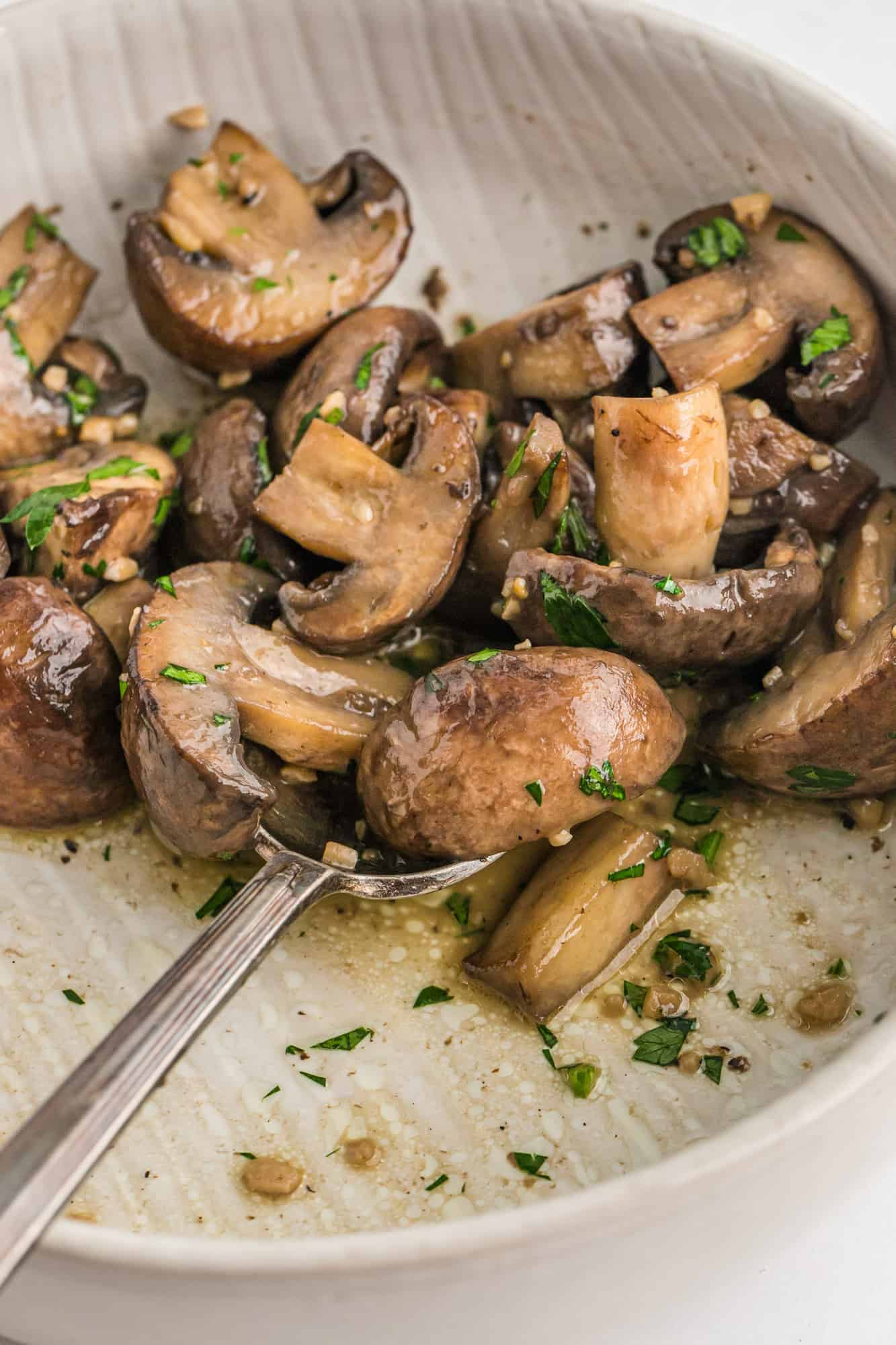 Mushrooms in a bowl with garlic butter and parsley.