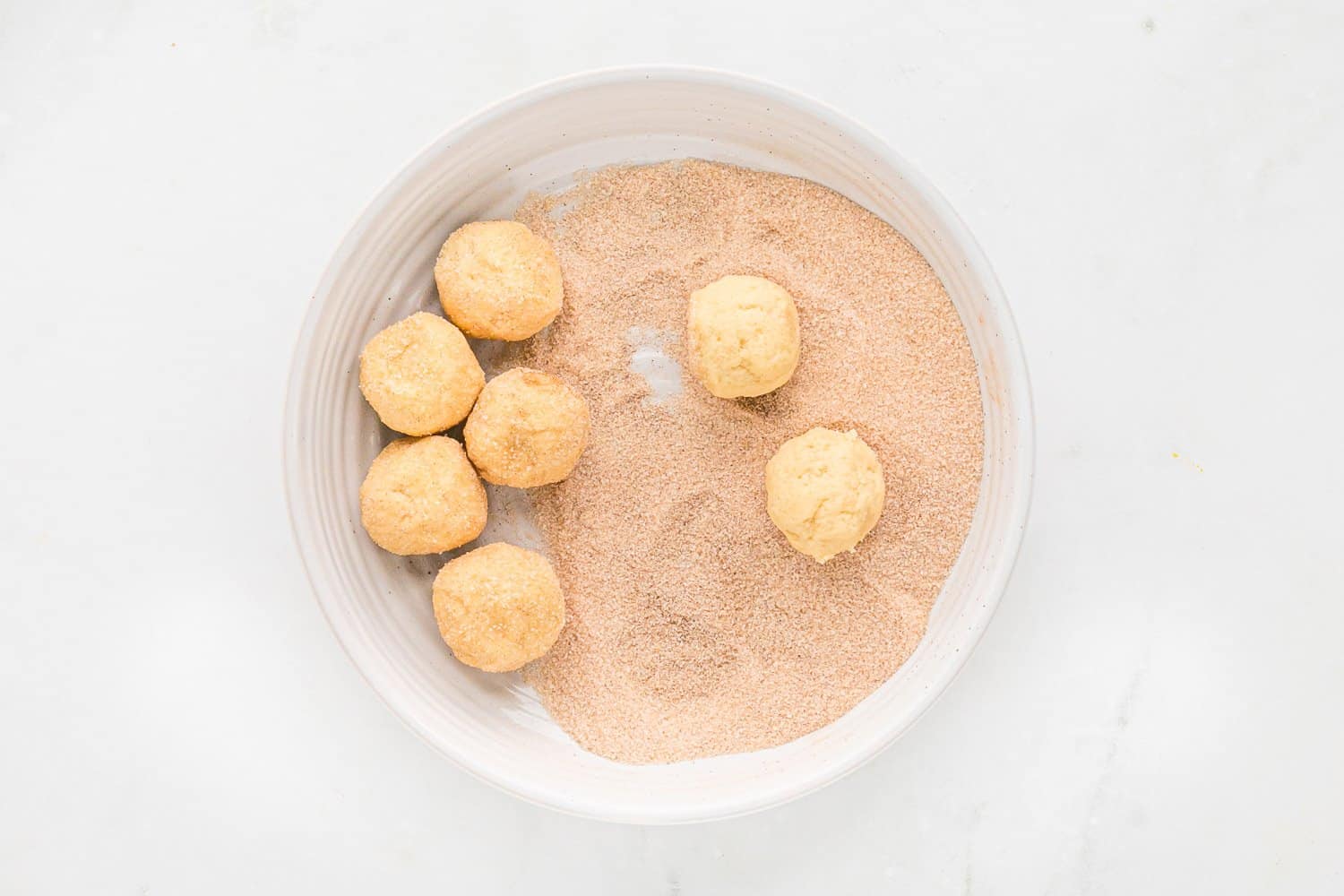 Cookie dough balls being rolled in cinnamon sugar.