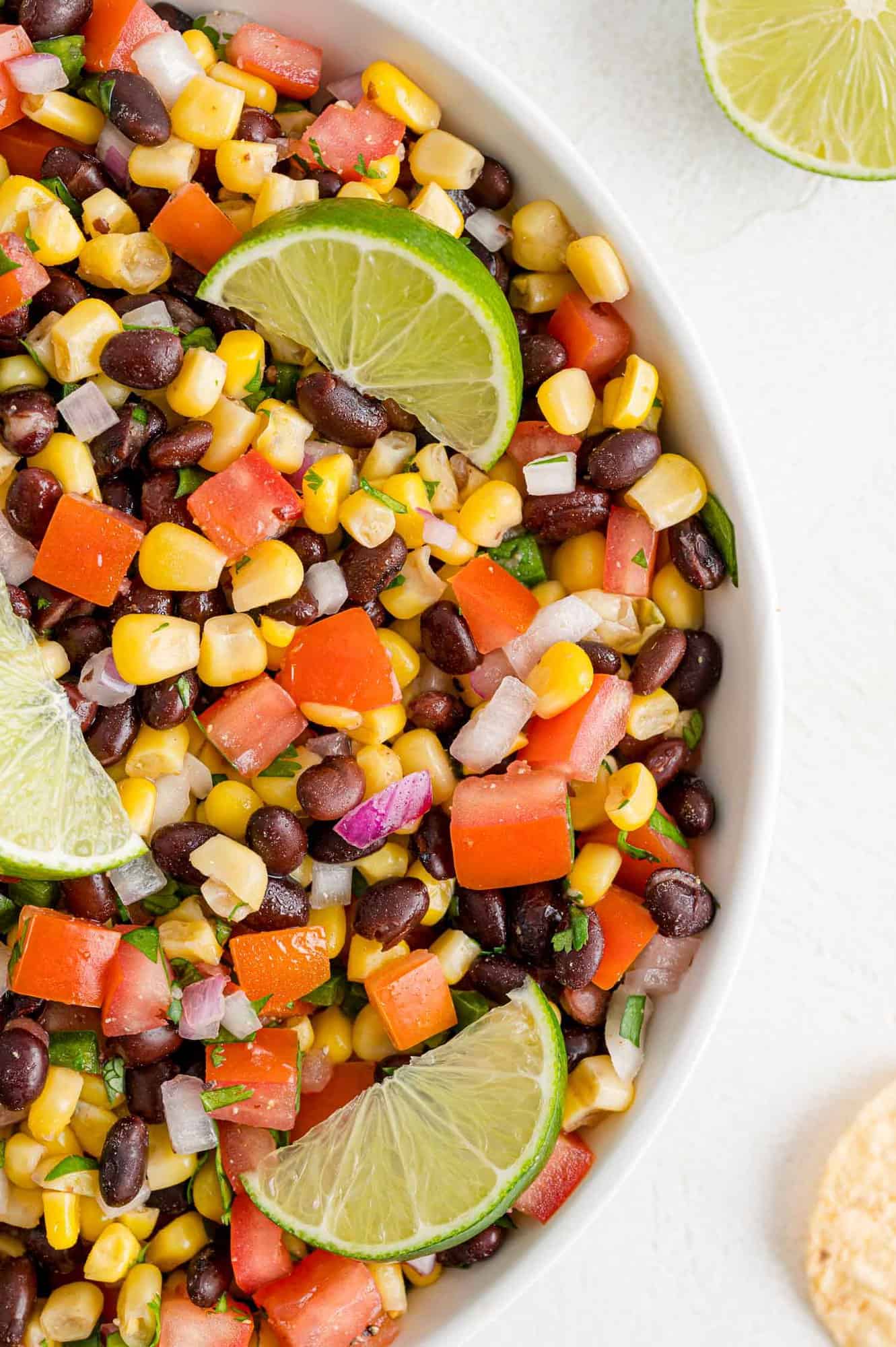 Bean, tomato, and corn salsa in a bowl with lime wedges.