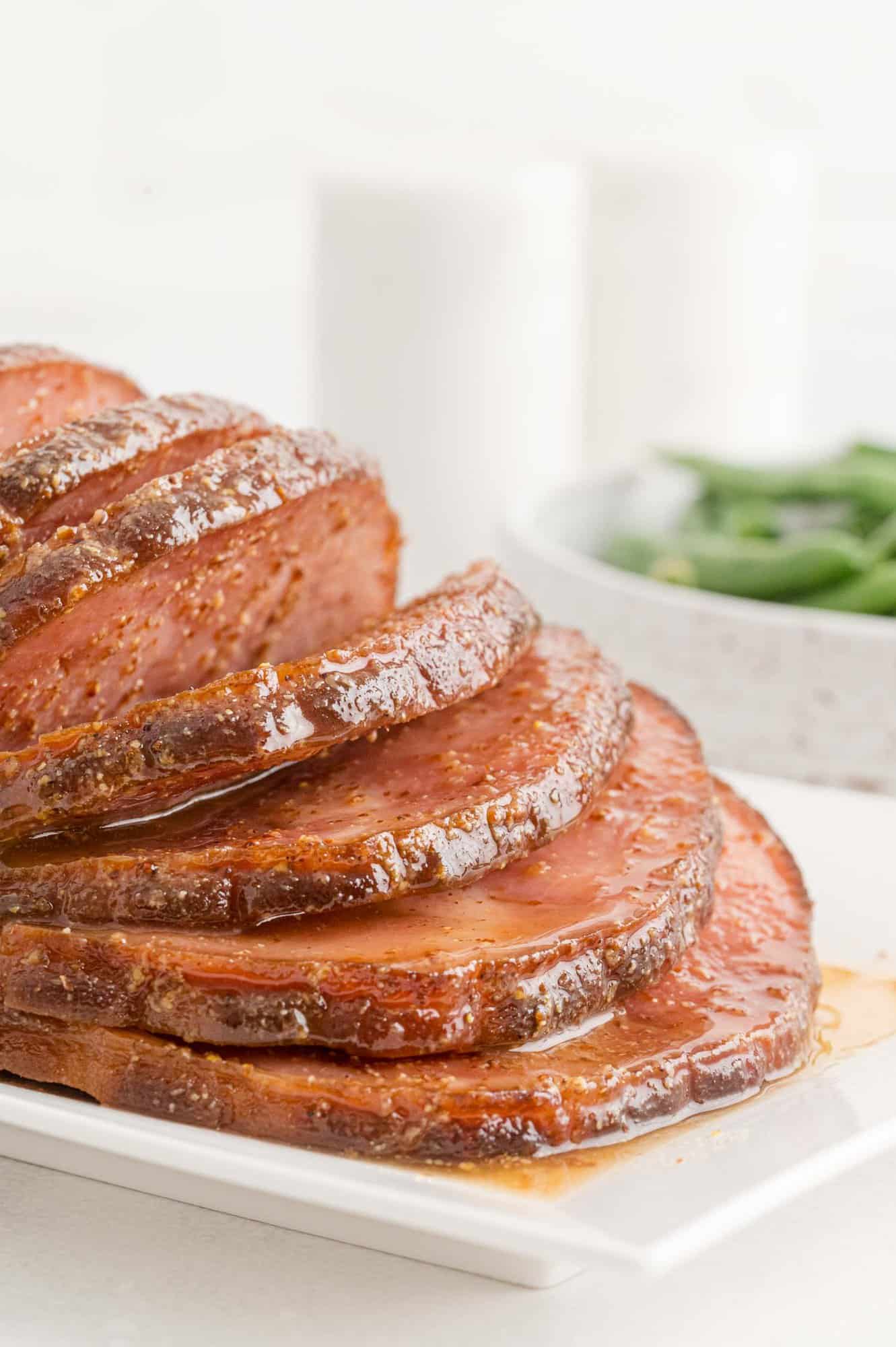 Crockpot ham sliced and on a plate with maple dijon sauce.