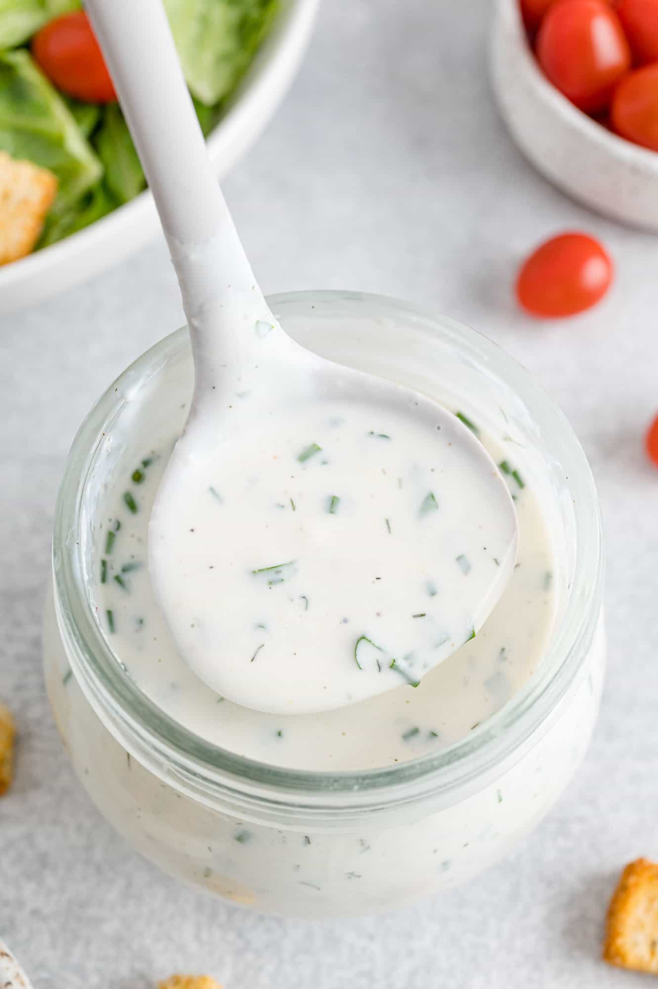 Homemade ranch dressing in a ladle held over a jar.