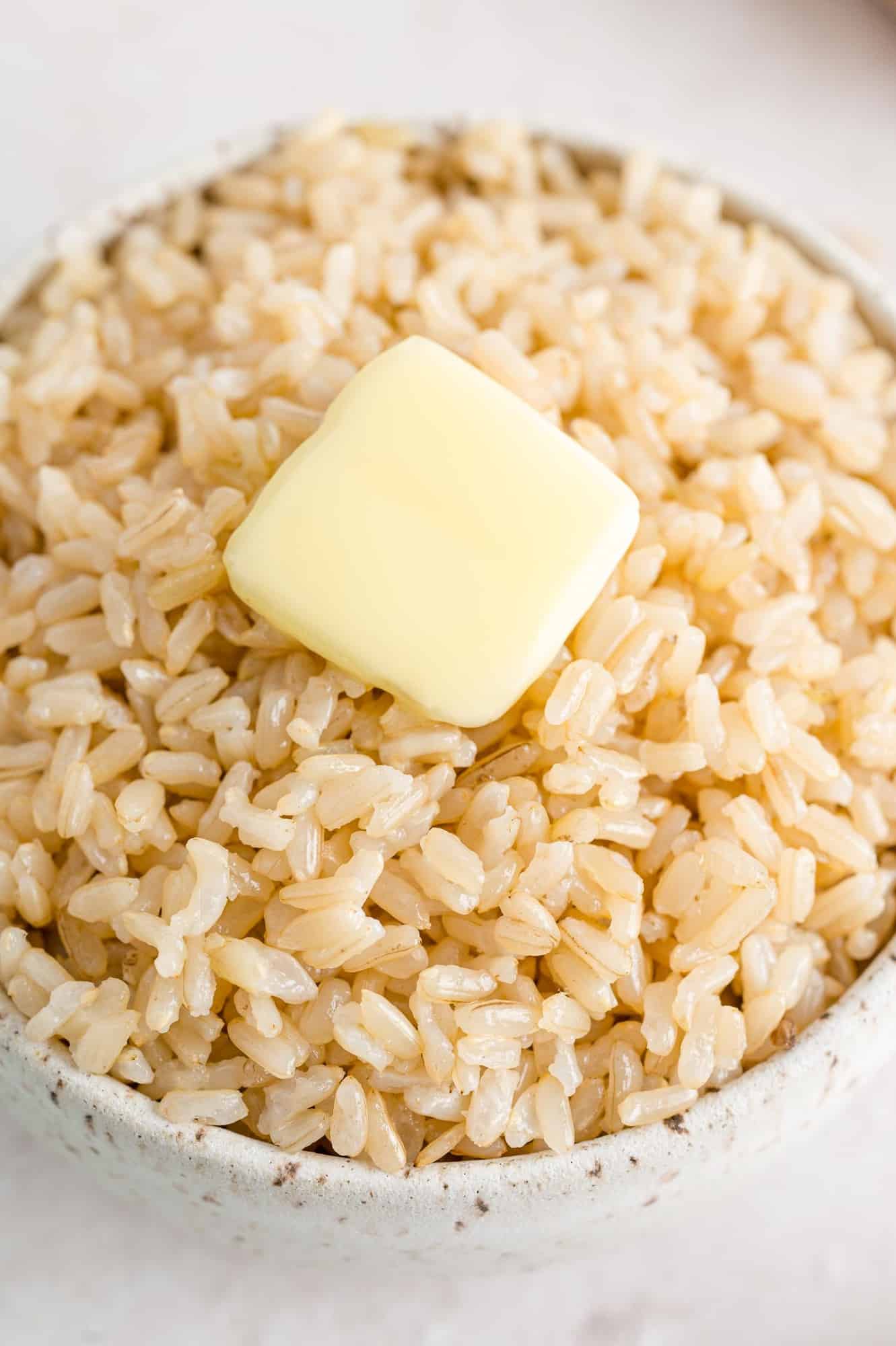 Close up view of brown rice and a pat of butter in a white bowl.