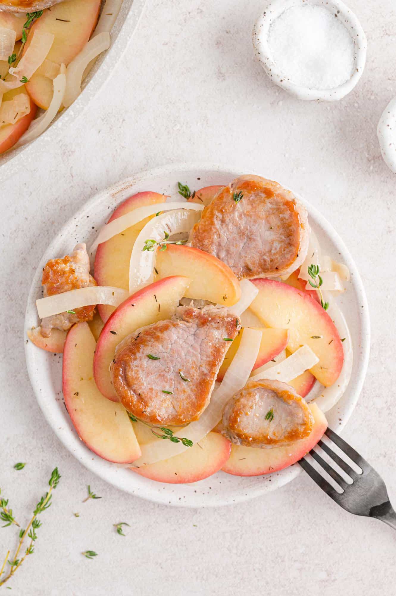 Pork, apples, onions on a white plate.