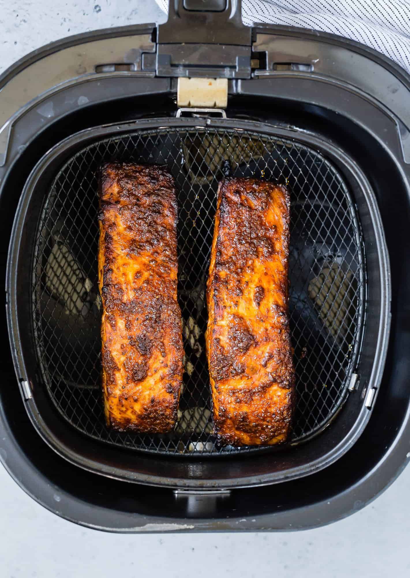Two salmon fillets in an air fryer basket.