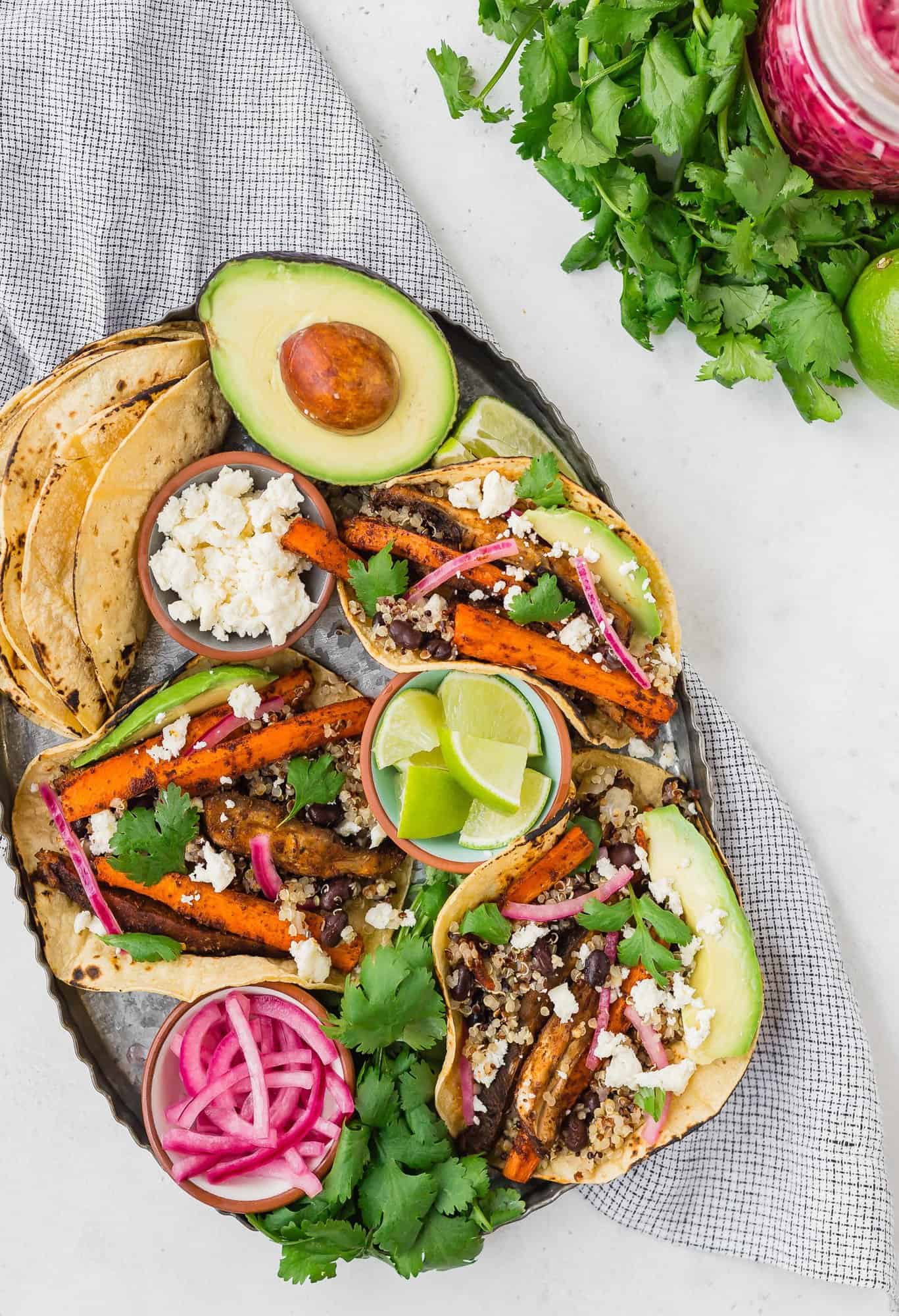 Tray of tacos, pickled red onions, cheese, limes, and more.