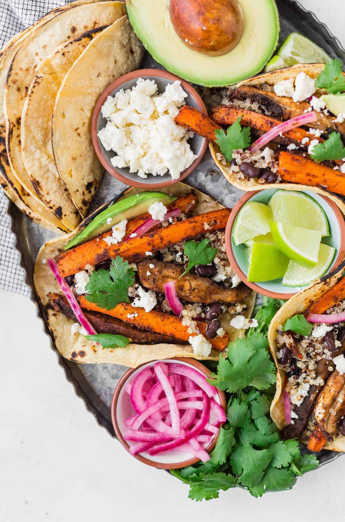 Carrot and mushroom tacos on a tray with toppings.