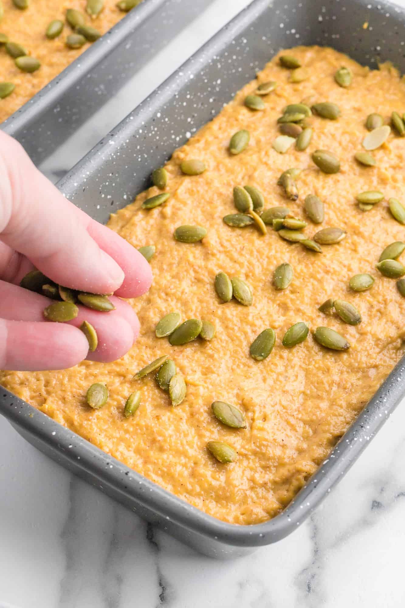 Pumpkin quick bread being sprinkled with pepitas.