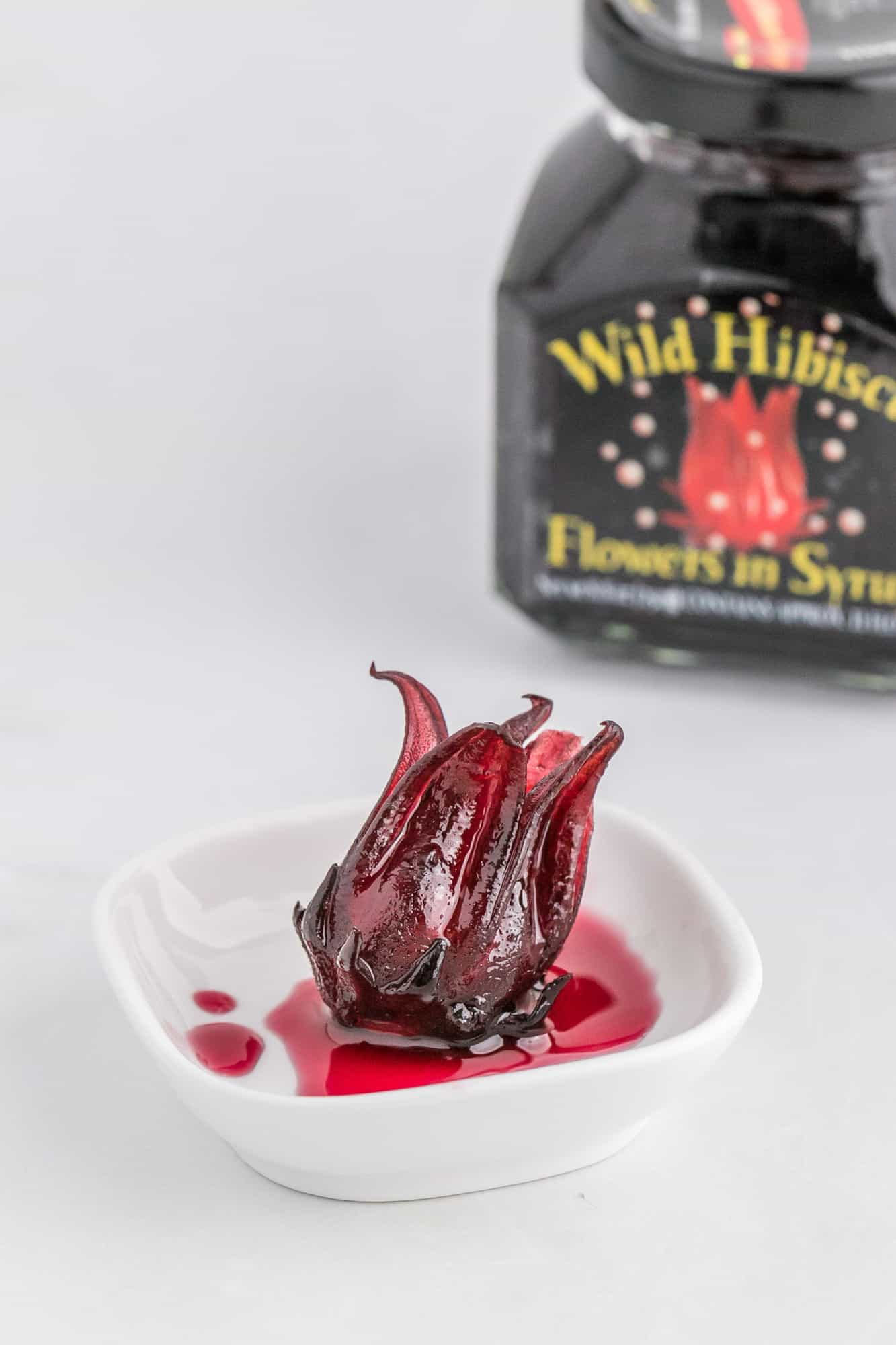 Hibiscus flower in a small white dish, jar in background.