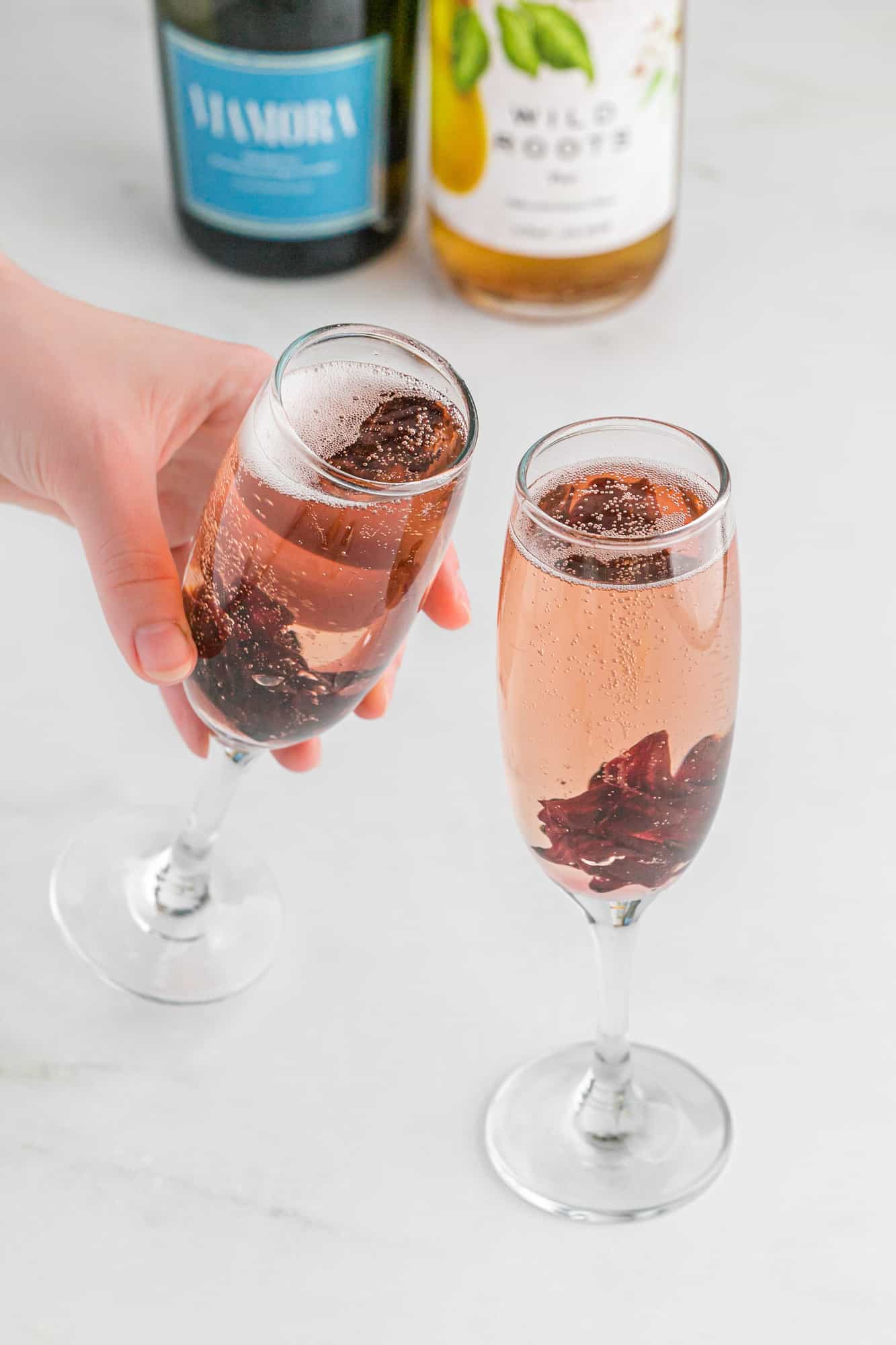 Two champagne flutes, one held in a hand, containing hibiscus mimosas.