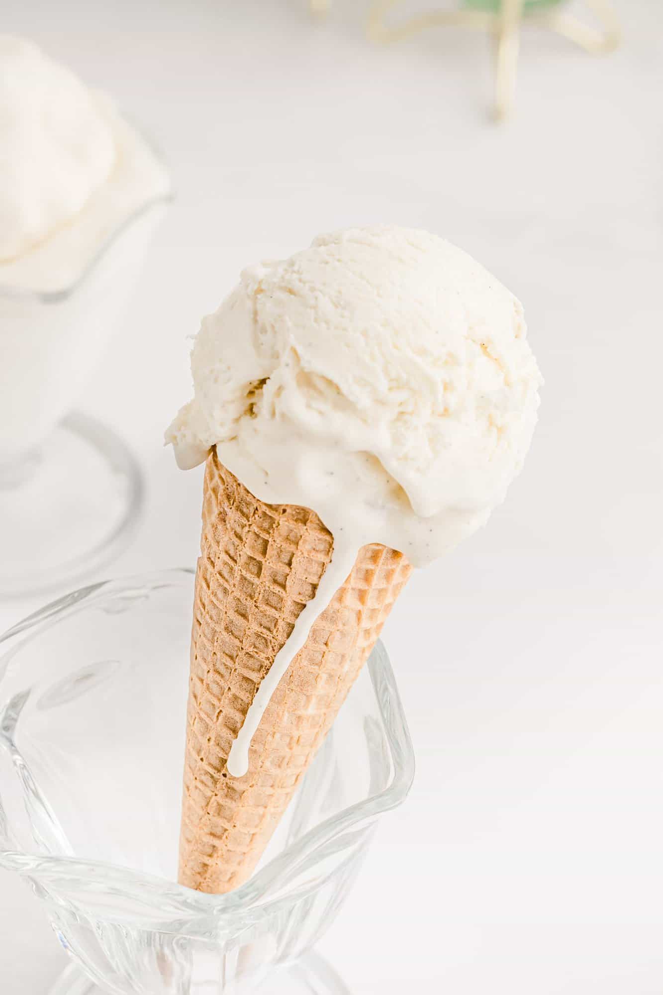 A scoop of vanilla ice cream in a cone, with melted ice cream dripping down the side.