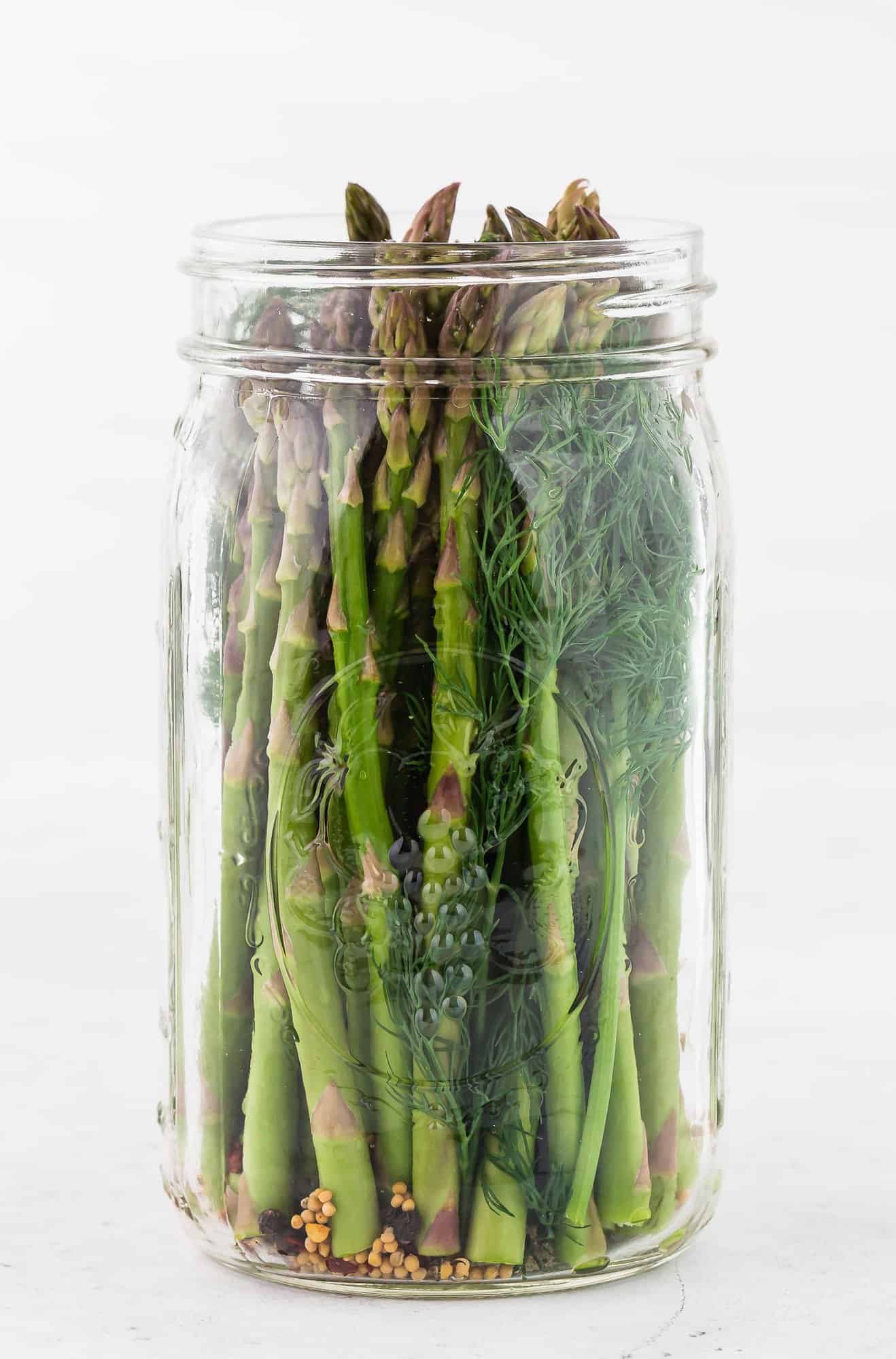 Pickled asparagus in a jar against a white background.