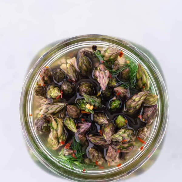 Pickled asparagus in a jar, photographed from above, showing the flowery ends of the asparagus spears.