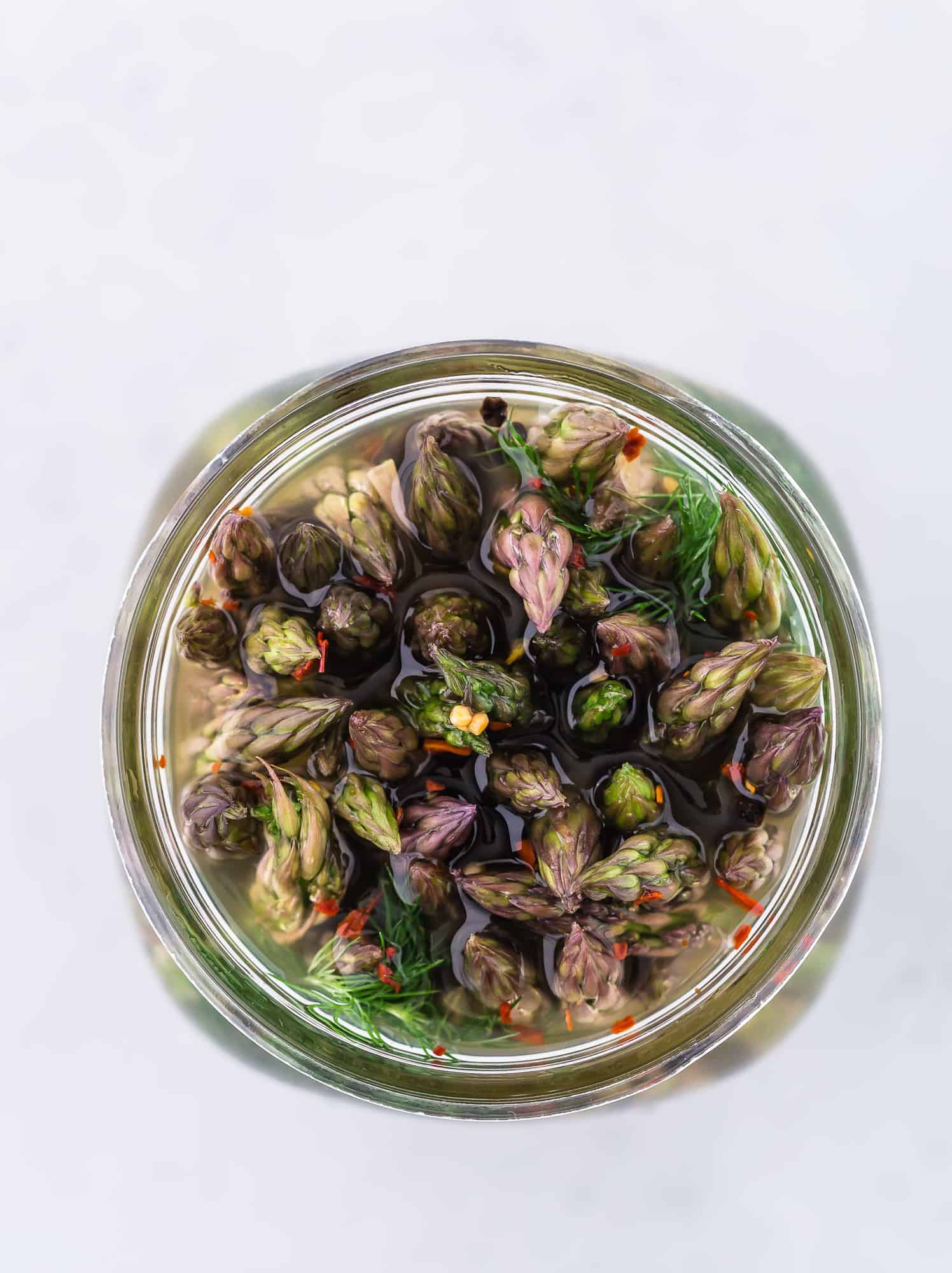 Pickled asparagus in a jar, photographed from above, showing the flowery ends of the asparagus spears.