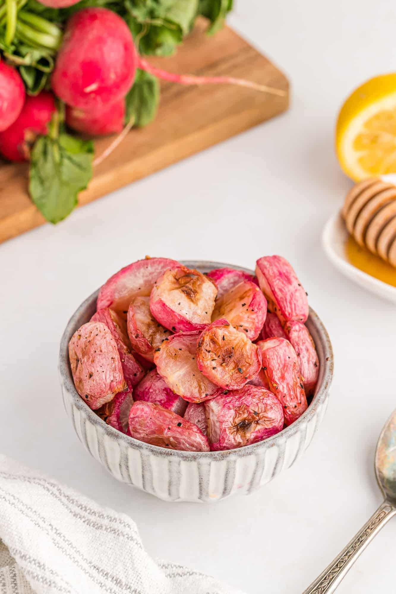 Radishes in a bowl with more in the background along with fresh lemon and honey.