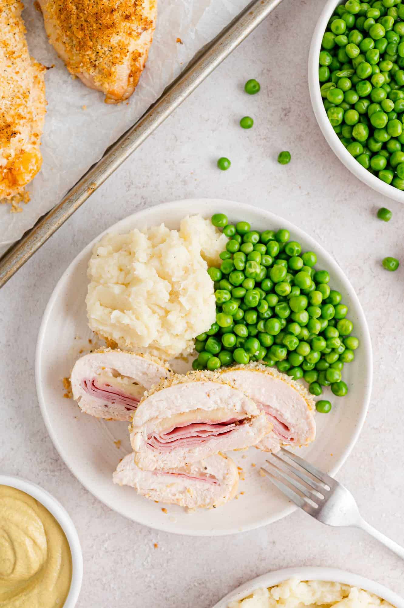 Sliced chicken cordon bleu to show filling, on a plate with peas and potatoes.