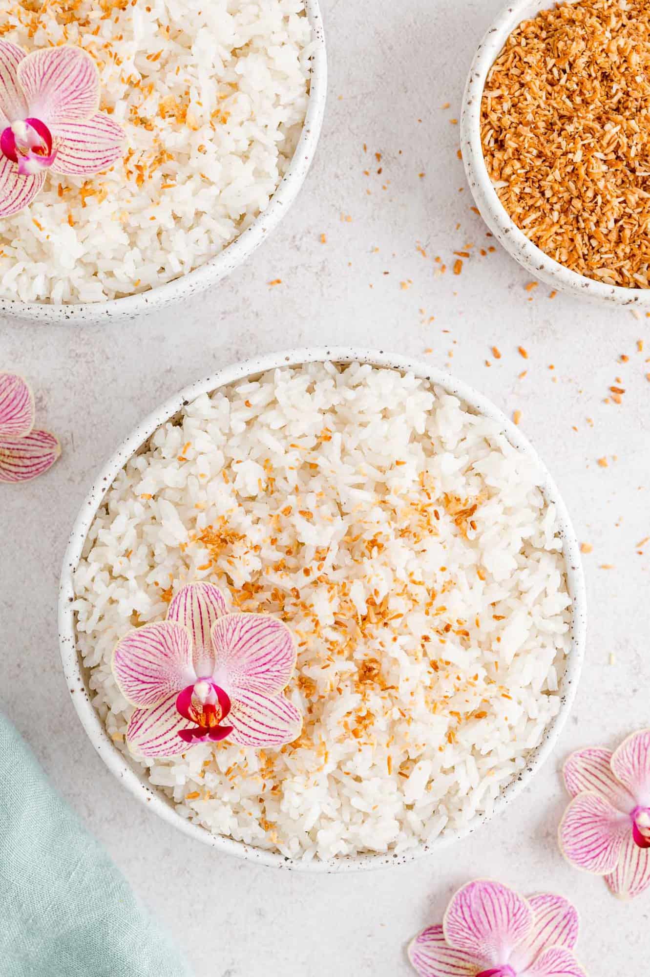 Coconut rice garnished with coconut flakes and a pink orchid.