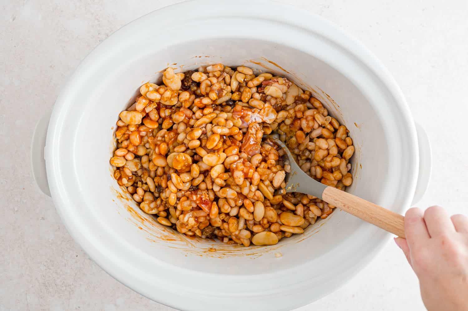 Ingredients being stirred together in a white slow cooker.