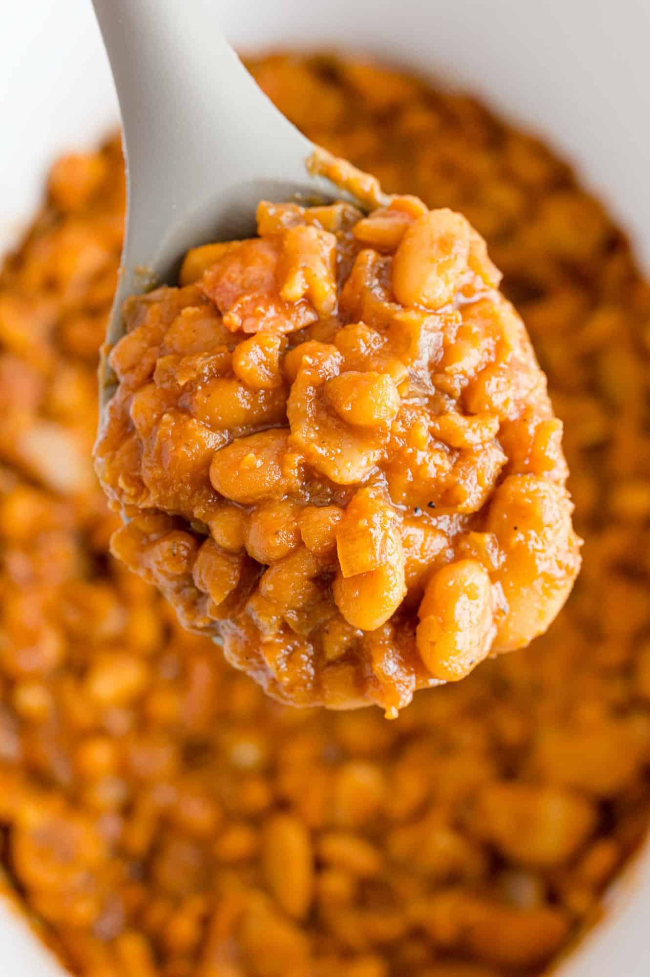 Spoon of crock pot baked beans held over more.