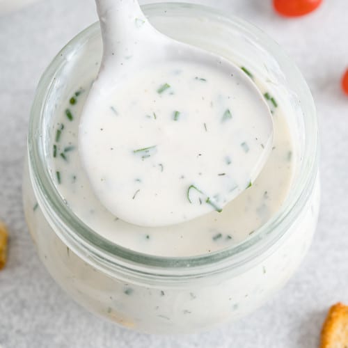 Healthy ranch dressing in a small ladle held over a jar.