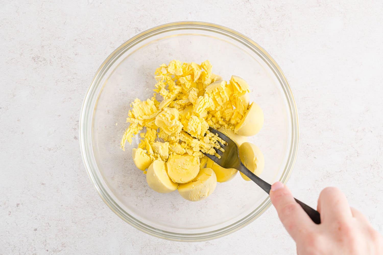 Egg yolks in a bowl, being mashed with a fork.