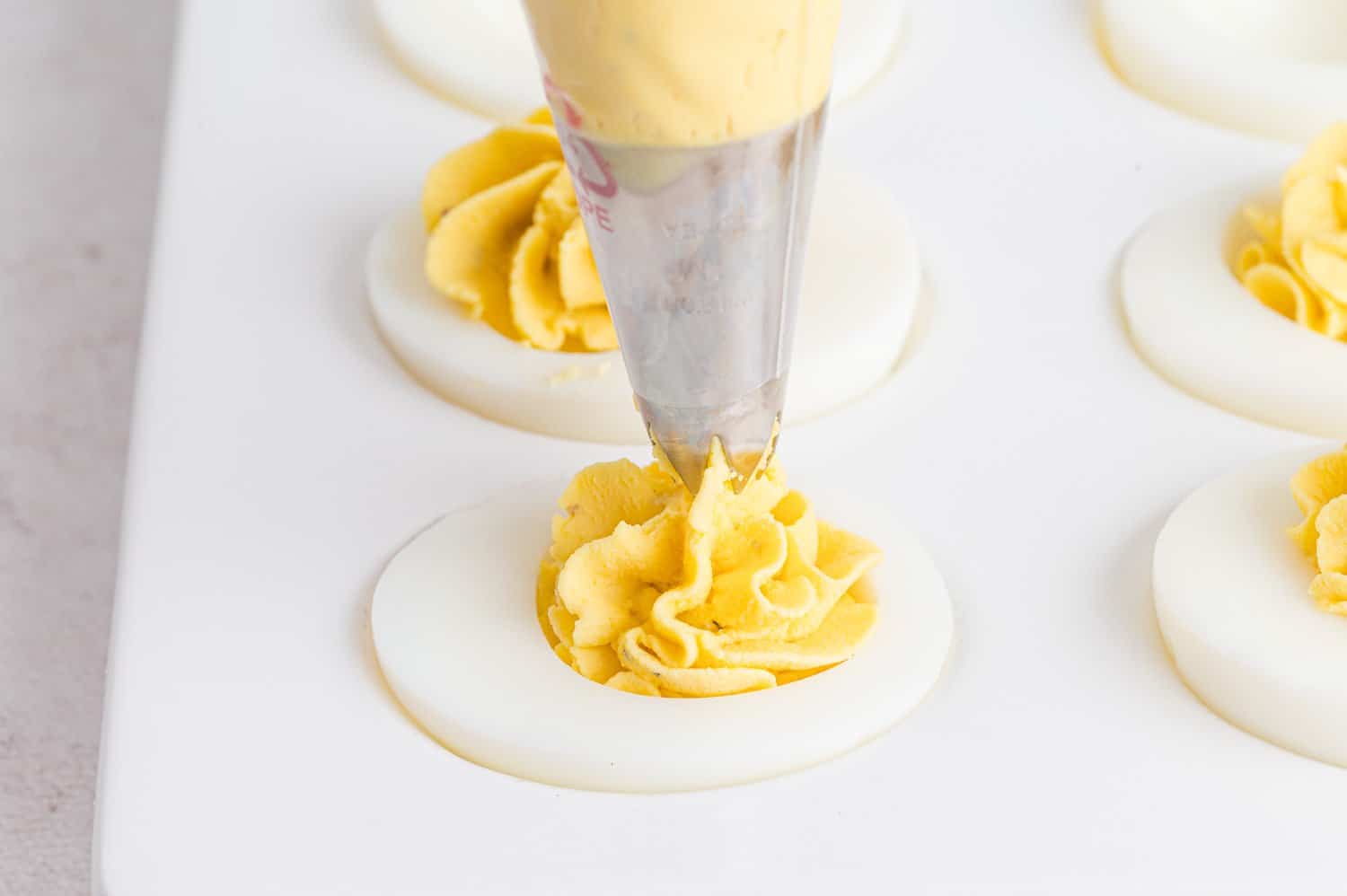 Deviled eggs being filled with a piping bag.
