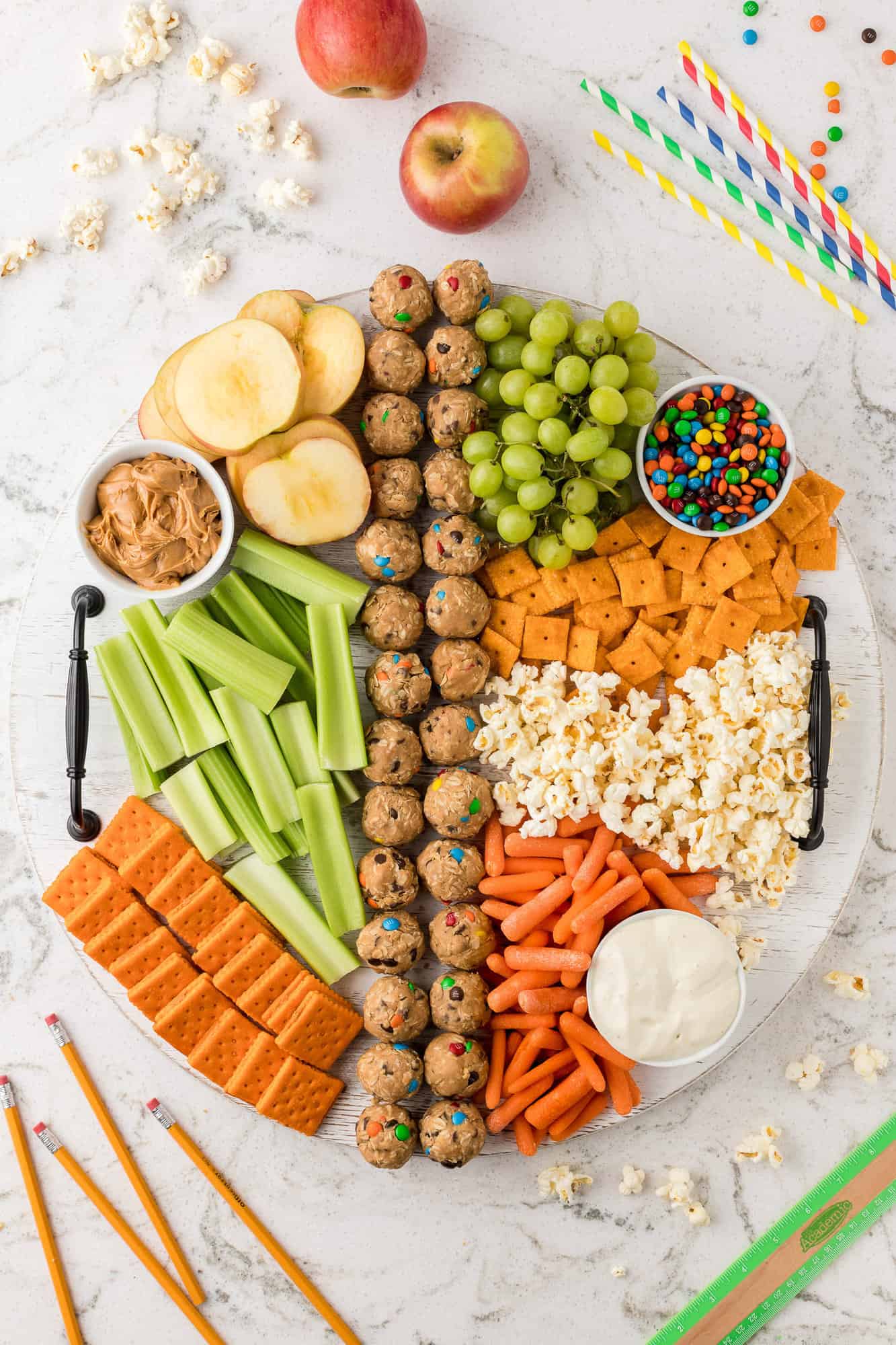 Snack board with crackers, snacks, fruit.