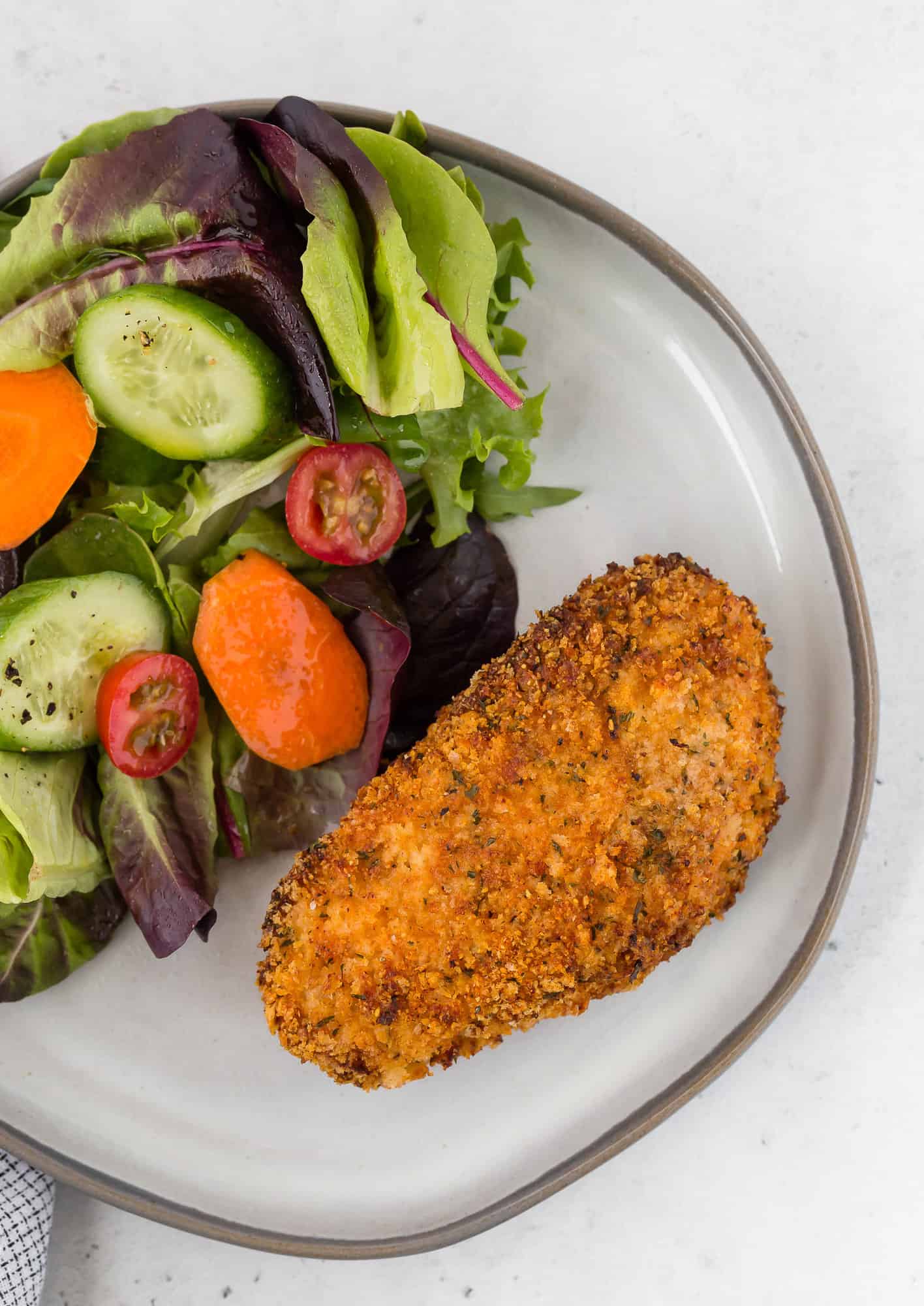 Overhead view of a breaded pork chop on a plate with a salad.