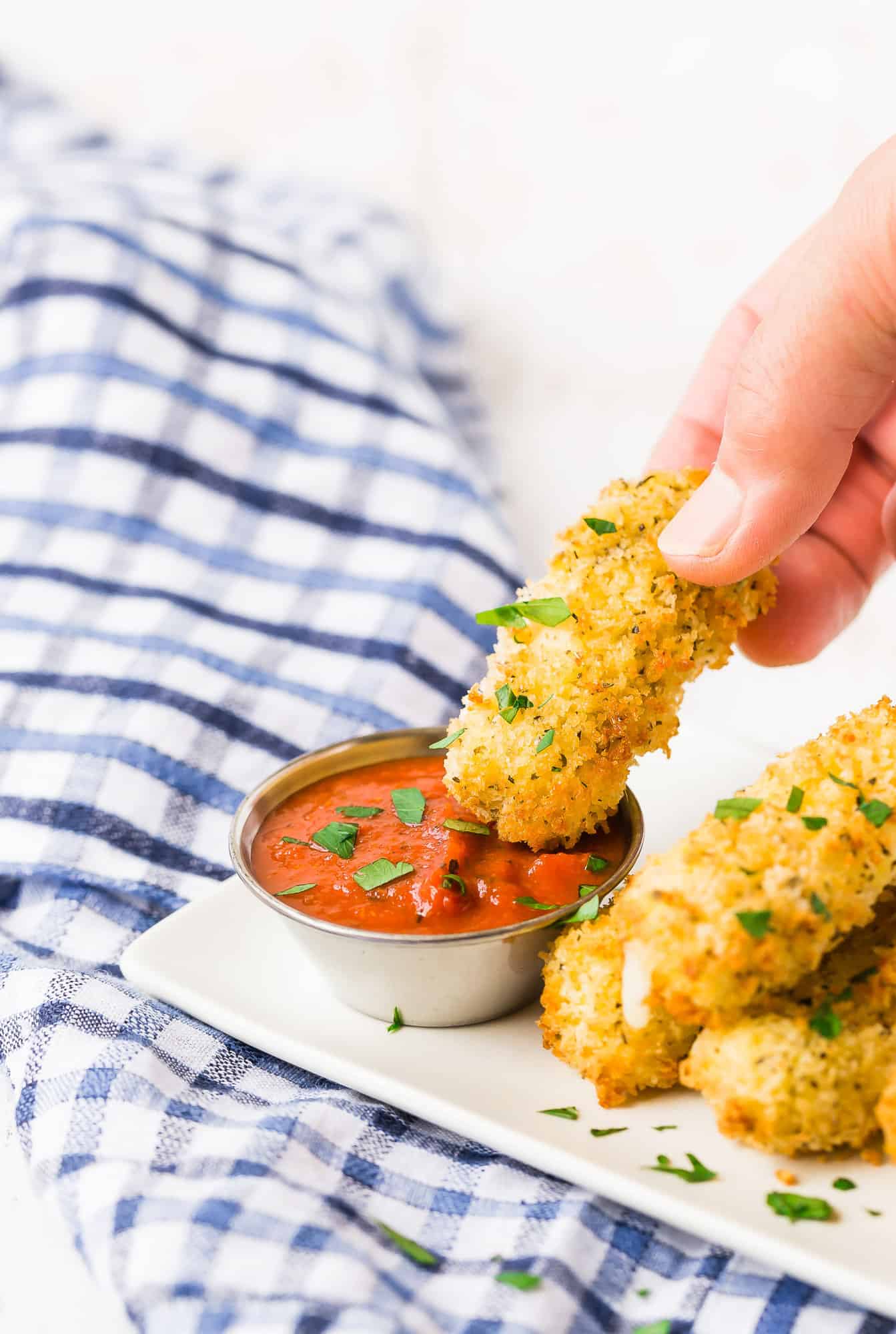 Mozzarella stick being dipped into pizza sauce.