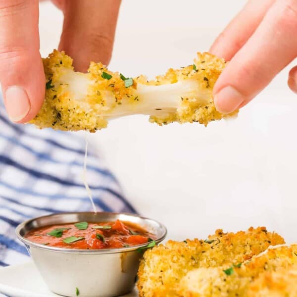 Air fryer mozzarella stick being pulled apart with a cheese pull.