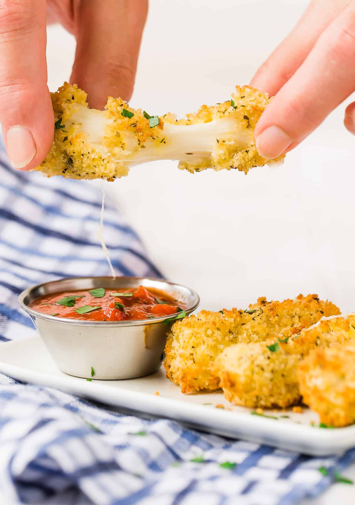 Air fryer mozzarella stick being pulled apart with a cheese pull.