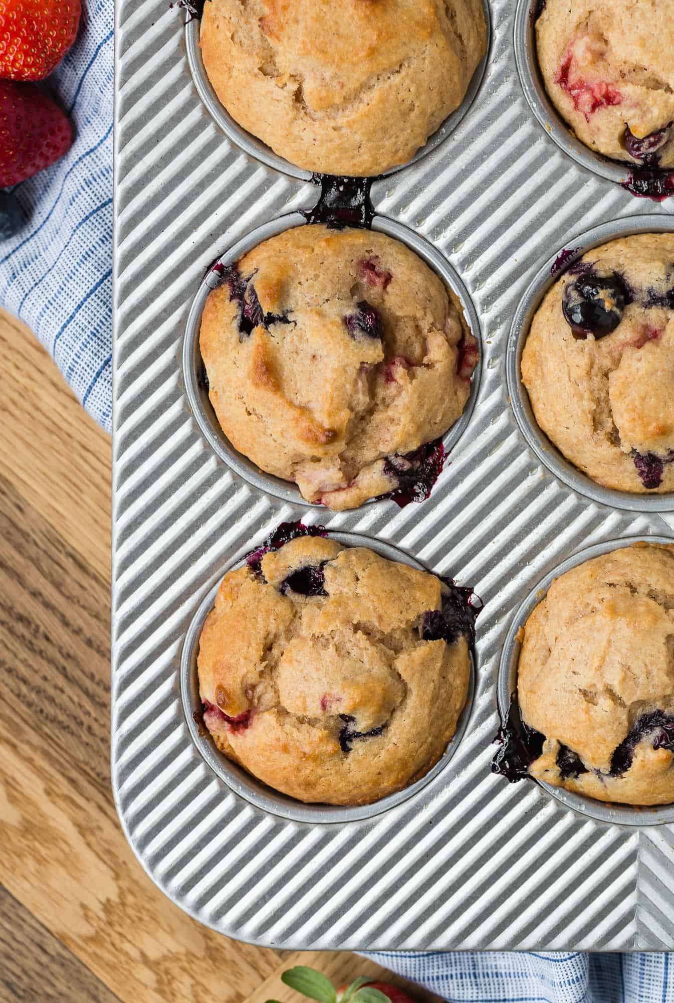 Muffin tin with muffins in it that are flecked with blueberries and strawberries.