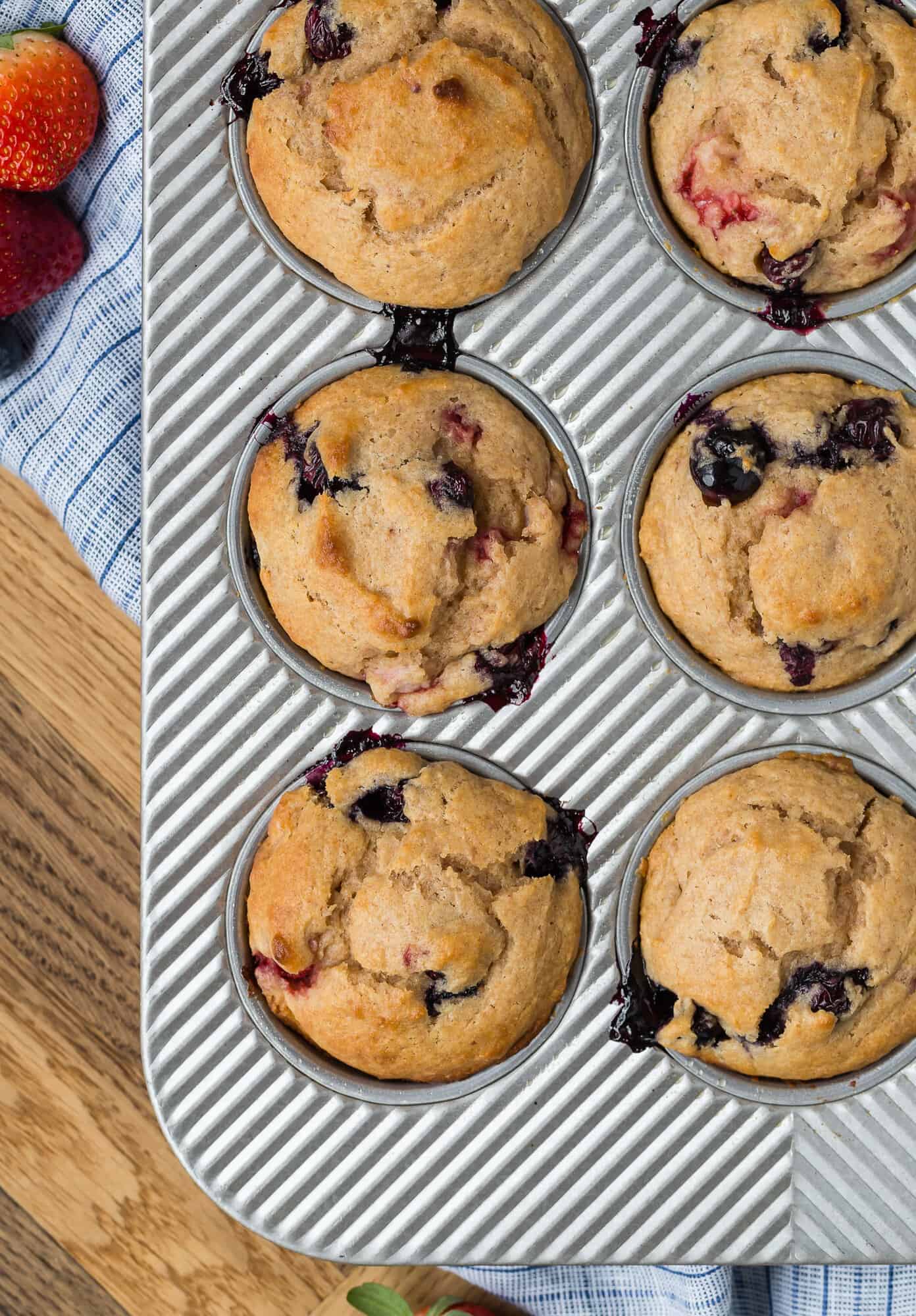 Muffin tin with muffins in it that are flecked with blueberries and strawberries.