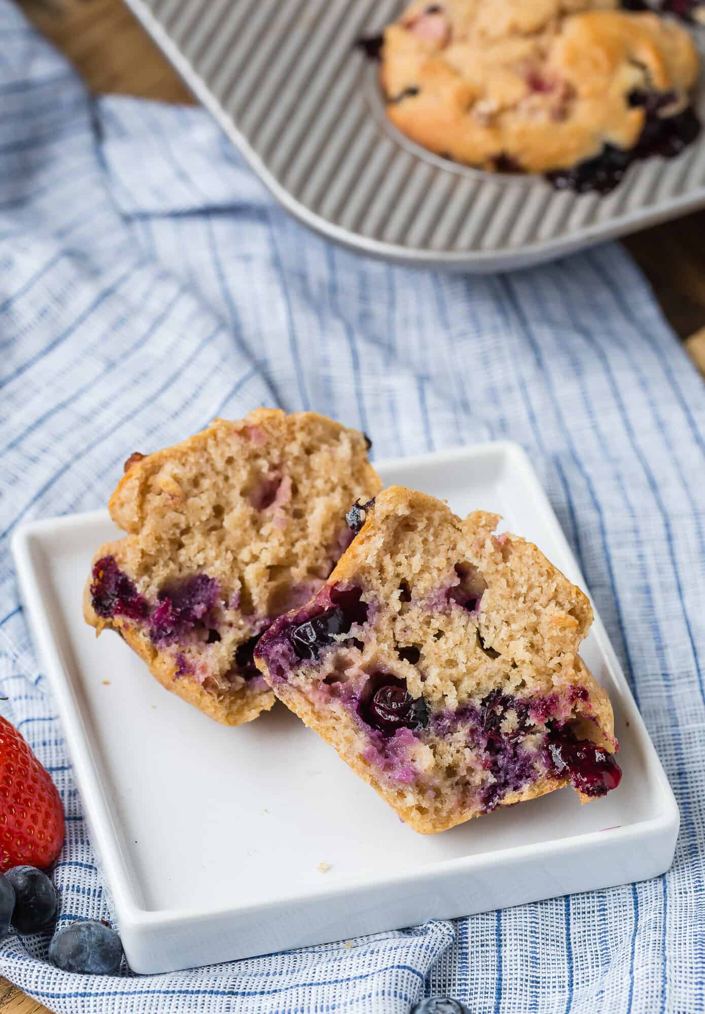 A muffin full of berries split open on a white plate to show the inside.