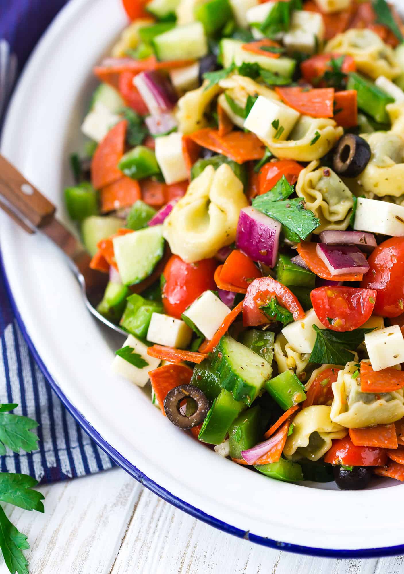 Tortellini pasta salad on a white plate with wooden spoon